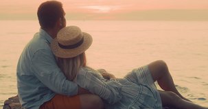 Fun attractive couple of traveler sitting on sea beach with ukulele under sunset sky in evening time. Man playing, woman listening and sing music, relaxing enjoying holidays, travel day. 4K video
