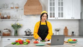Woman housewife in apron slices cucumber on cutting board, listen teacher chef study online video call conference webcam chat laptop computer, distance education culinary course lesson in home kitchen