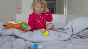 Little girl with blond hair playing on the bed, picking up and moving bright plastic shapes