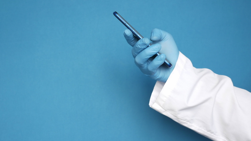 doctor's hand in protective gloves using a smartphone against blue bakcground