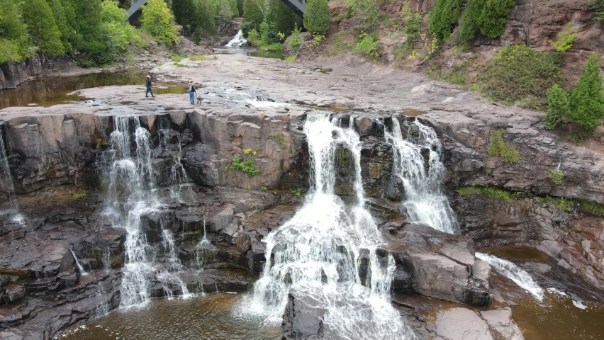 Aerial clip panning up Gooseberry waterfalls. Waterfalls surrounded by rocky landscape and forested area. Near Duluth, MN. Outdoors, summer.