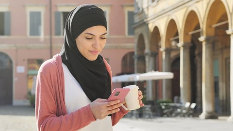 young muslim woman wearing hijab headscarf using smart phone walking in the city center,arab girl holding smartphone mobile texting messaging,online shopping communication,social network concept