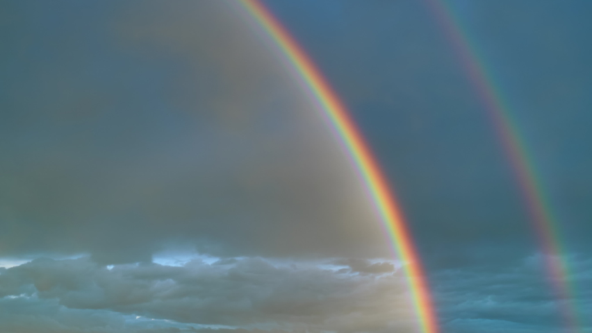 Time lapse of intense double rainbow on dark blue sky after rain. Timelapse,  light rays, copy space.