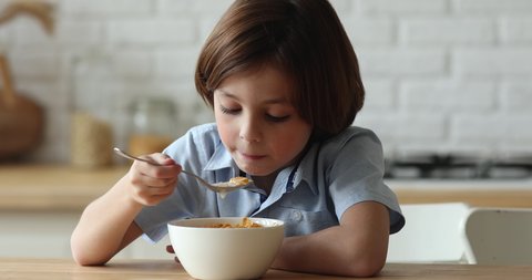 Close up little hungry cute boy sit at dinner table eat cornflakes with milk with pleasure appetite, enjoy balanced food, whole grain dry cereal for breakfast. Nutrition, tasty snack for kids concept