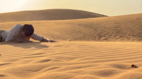 A man in an office cloth crawls up a dune in a desert. Overcoming challenges in business