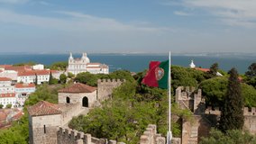 Close-up of national and municipal flags on poles over medieval stone Saint George Castle. Drone camera flying backward away from landmark. Lisbon, capital of Portugal. - Powered by Shutterstock - Get 15% off with code: PIKWIZARD15