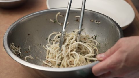 White Pasta With Herbs Toss In A Silver Bowl Using Tongs. - High Angle Shot