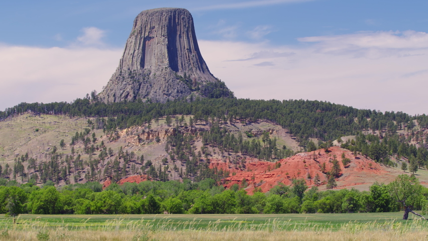 View of Devils Tower across field as grass blows in the wind in Wyoming as clouds move on the horizon.