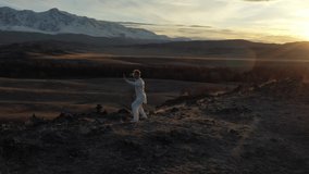 Video of kungfu master in a white sports uniform training on the hill. Man perform wushu forms in nature on background of snowy mountains at sunset time.