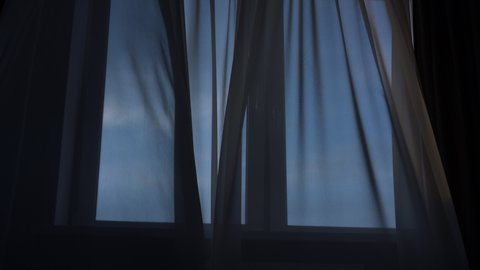 Strong wind blowing in open window and swaying thin curtain in living room
