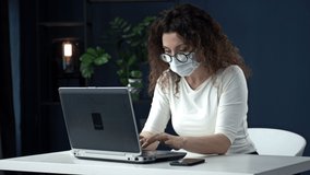 Work during the coronavirus epidemic. Tired middle-aged business woman takes off her glasses, a medical mask and closes her laptop in relief at the end of the working day.