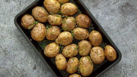 Oven baked whole potatoes with seasoning and herbs in metalic tray. Roasted potatoes in jackets.