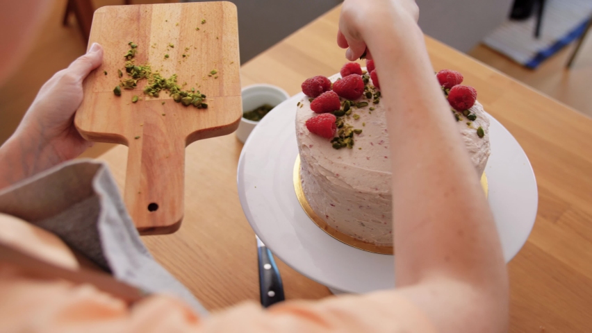 culinary, baking and cooking food concept - woman decorating raspberry cake with pistachio and on kitchen at home