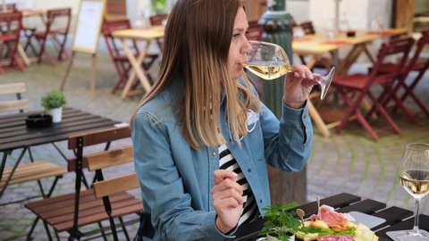 A young beautiful woman drinking white wine or Prosecco at a bar or restaurant on the street. aperitif food antipasti with prosciutto and salami, glass of Prosecco or white wine