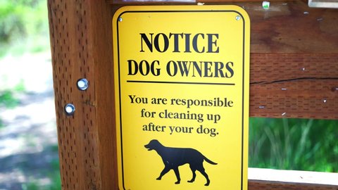 Notice to Dog Owners you are responsible for cleaning up after your pet bright yellow sign at public park hiking trail, panning back and forth keeping sign in frame, in 4k slow motion.