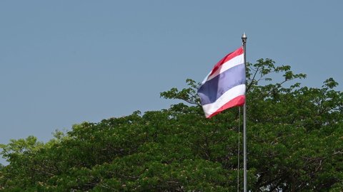 Muak Klek , Saraburi , Thailand - 04 16 2021: A lengthy clip of a Thai Flag flying during a windy sunny day against a tree and blue sky, perfect for adding the national anthem.