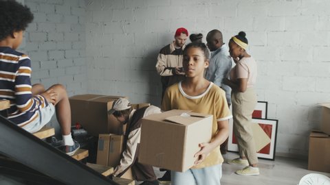 Slowmo tracking shot of male movers delivering cardboard boxes to African-American family in empty house or apartment Black man using debit card to pay workers