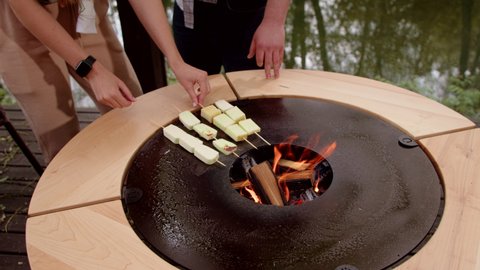 Fry halloumi cheese on the grill. A guy and a girl are preparing cheese on a round designer grill. Close-up of frying cheese on the surface of the grill.