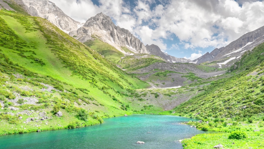 Paradise mountain lake with the rapid movement of clouds across the sky with falling shadows on the hills. Timelapse of a high-mountain lake in spring in cloudy weather
