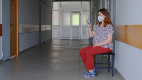 Pregnant woman with phone in hospital corridor with medical mask on face n95