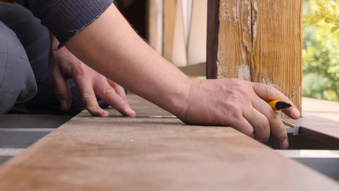 Repair home. Flooring installation a terrace. Carpenter draws a cutting line on wood plank. Close up measuring floorboards with corner ruler. Joiner with pencil and meter marks measure on wooden board