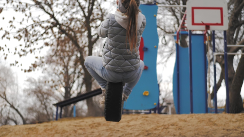 Happy child swinging on a car tire used as a swing. Active child girl playing on swing wheel in forest. Outdoors activity for kids. Preschool child having fun and swinging.
