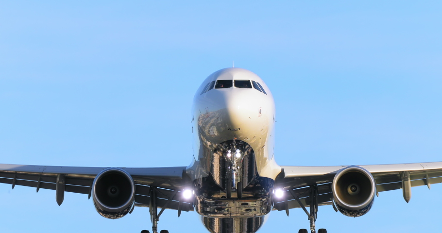 Cinematic travel background. Landing airplane flying above camera at sunset or sunrise in clear blue sky. Front view of large jet taking off international airport. Vacation 4K slow motion footage