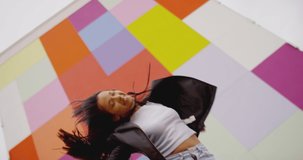 4K Beautiful , stylish , young girl with black hair  beautiful body in Leather Jacket and sport jeans  dancing , moving , smiling and looking at camera with happy emotions . Slow motion colorful wall