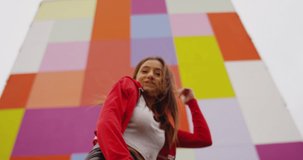 4K Beautiful , stylish , young girl with blond hair and beautiful body in Leather tights dancing , moving , smiling and looking at camera with happy emotions . Slow motion . Colorful wall background