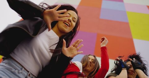 4K Three young beautiful , happy girls dancing , moving , looking at camera . Stylish bloggers in sport outfit  having fun , jumping and shaking body in front of colorful background wall . slow motion