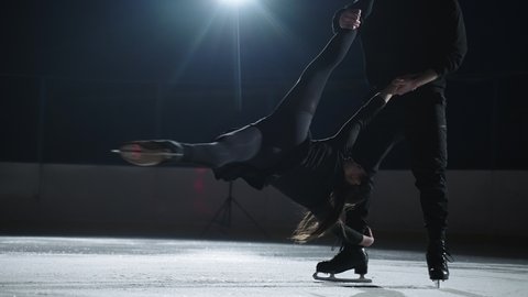 Pair figure skating on the rink. A man and a woman in a counter-light perform elements of the Olympic program together in slow motion