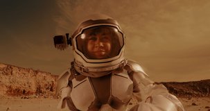 Low angle of happy woman in spacesuit speaking and gesticulating while shooting video during colonization of Mars