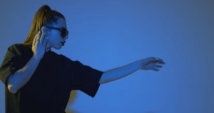 Stylish young fashion girl in sunglasses cool dancing in blue neon studio light. Modern hip hop dance. Copy space