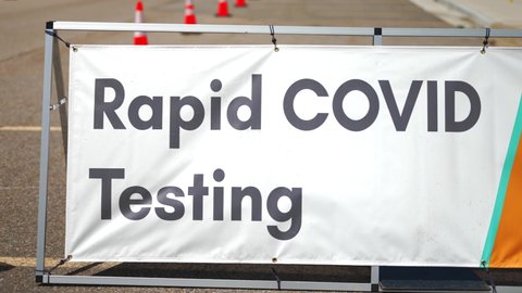 Rapid Covid-19 Testing site sign posted outside on sunny and hot summer or spring day (2021) in empty parking lot with orange cones setup. Slow panning from right to left, in 4k slow motion.