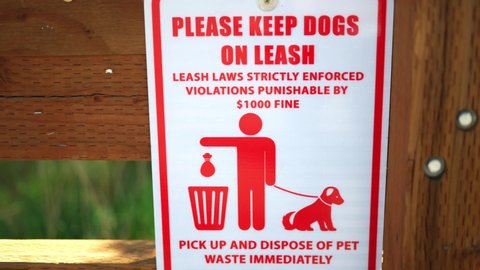 Please keep dog on leash, laws strictly enforced, violations punishable by $1000 fine, and pick up your pet waste poop sign, posted at public national park hiking trail. In 4k slow motion.
