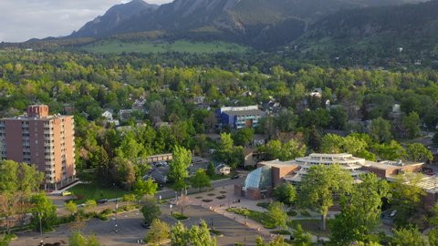 Aerial pan up reveal of beautiful flatiron mountain vista and bright green trees in Boulder Colorado during an evening sunset with warm light on the rocky mountain town and summer landscape