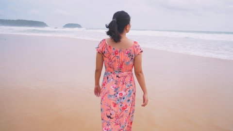 Asian woman walking on deserted beach in late afternoon.