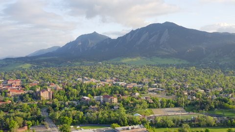 Aerial pan left of beautiful flatiron mountain vista, bright green trees, and CU Boulder campus in Boulder Colorado during an evening sunset with warm light on the summer landscape