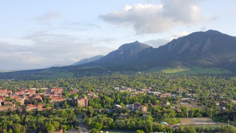 Aerial shot of beautiful flatiron mountain vista, bright green trees, and CU Boulder campus in Boulder Colorado during an evening sunset with warm light on the summer landscape