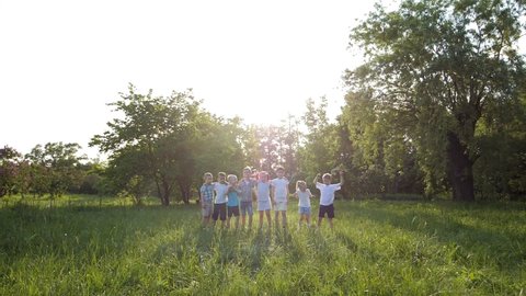 Slow-motion video. A group of children, friends of boys and girls, are standing in the park on a sunny summer day in a green meadow, A group of little friends are hugging. Primary school children
