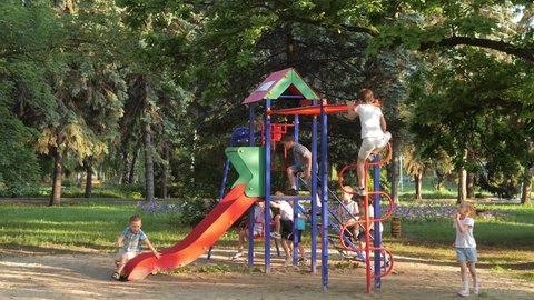Slow-motion video. A group of children, friends of boys and girls, play on the playground in the park. Children have fun in the park, hanging on their hands like monkeys