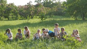 Slow-motion video. A group of children, friends of boys and girls, sit in the park on a sunny summer day in a green meadow and eat sandwiches. The concept of a child's dream. Primary school children