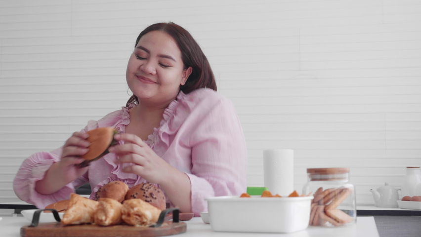 Young asian woman fat hungry and eating bread in the kitchen at home, female eat unhealthy food with delicious, girl obesity having appetite while overweight, dieting and health care concept. Royalty-Free Stock Footage #1074286889