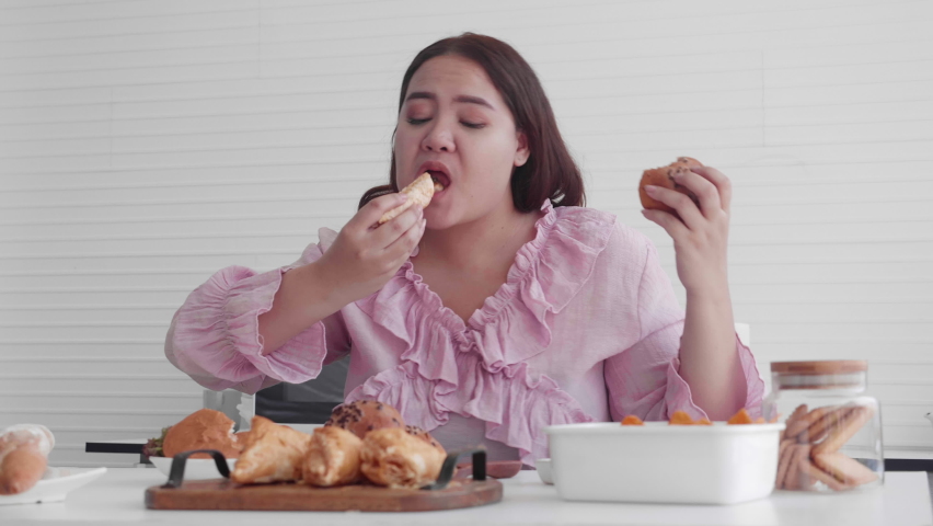 Young asian woman fat hungry and eating bread in the kitchen at home, female eat unhealthy food with delicious, girl obesity having appetite while overweight, dieting and health care concept. Royalty-Free Stock Footage #1074286889