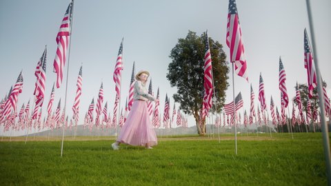 Young woman walking between flagpoles on summer day. Model celebrating Independence or Labor day in the green park with many American flag hanging down. Independence and Freedom concept 4K footage