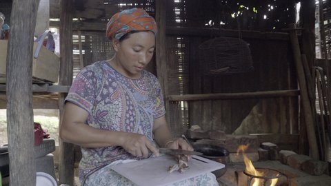 Imphal , Manipur , India - 04 15 2019: Manipuri woman cuts tough, rubbery hog ear for chutney near cook fire
