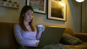 Asian woman drinking hot milk mug while watching online film on laptop at night before bed time