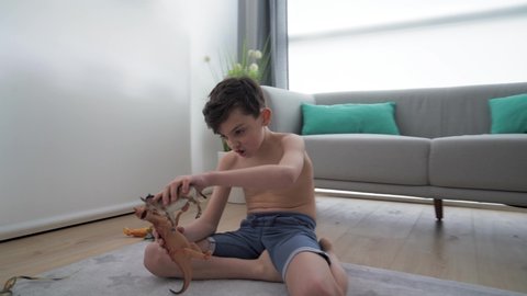 Boy sitting on carpet at home, playing with dinosaur toy figurines