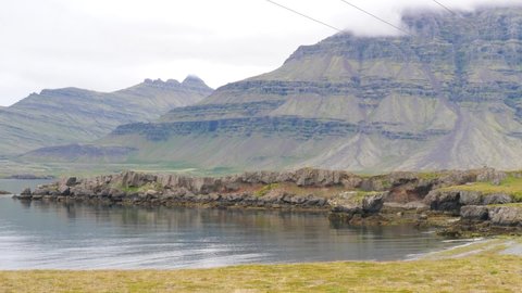 Berufjordur fjord terrain in eastern Iceland with strata on mountain edges with electric utility wires, Pan left shot