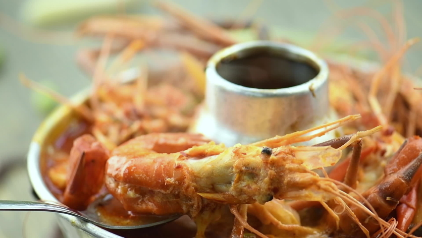 Tom Yam Kung or Tom Yum soup is Thai hot spicy soup shrimp or prawn with lemon grass, lemon, galangal, mushrooms, coconut milk and chili in bowl on wooden table top view, famous Thai food cuisine.